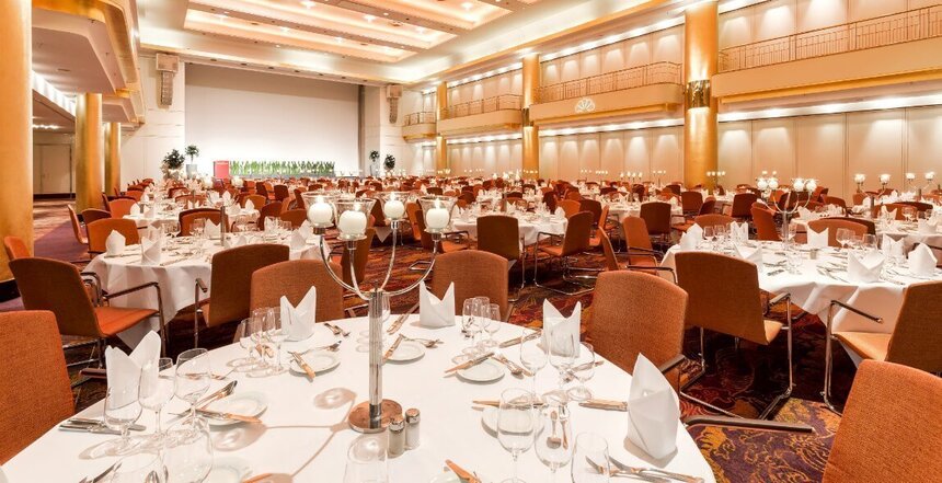 Großer  Festsaal mit edel gedeckten Rundtischen und hohen, goldenen Decken