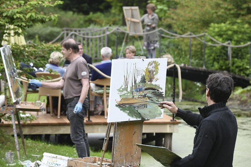 Einige Personen stehen in der Natur und malen mit Pinseln die Umgebung nach