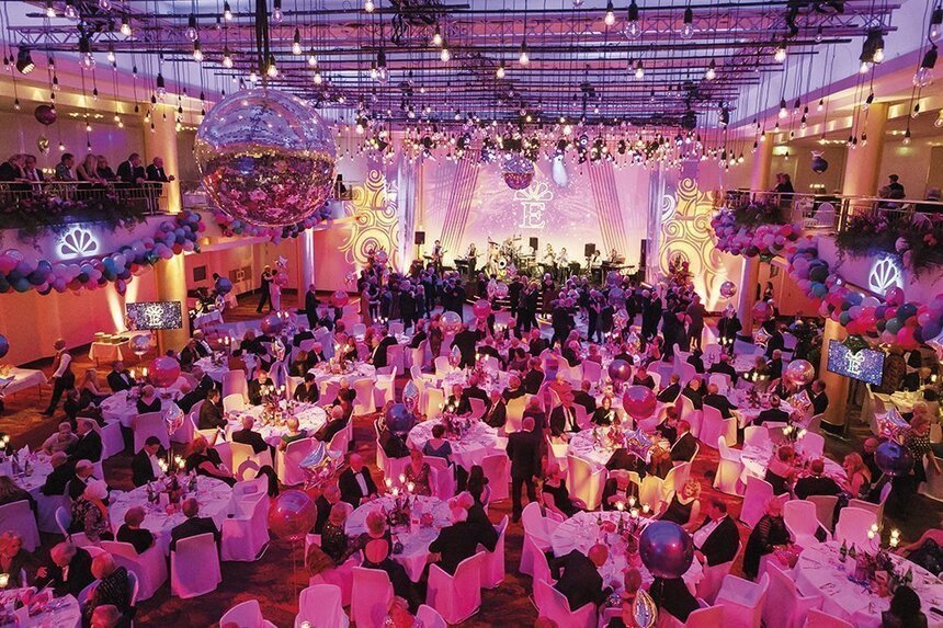 Festlich geschmückte Eventlocation mit Discokugeln und Lichtern an der Decke und zahlreichen Gästen an weißen Tischen