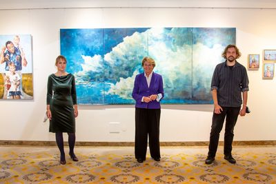 Drei Personen stehen in einer Kunstaustellung vor einem blauen Bild mit Wolken