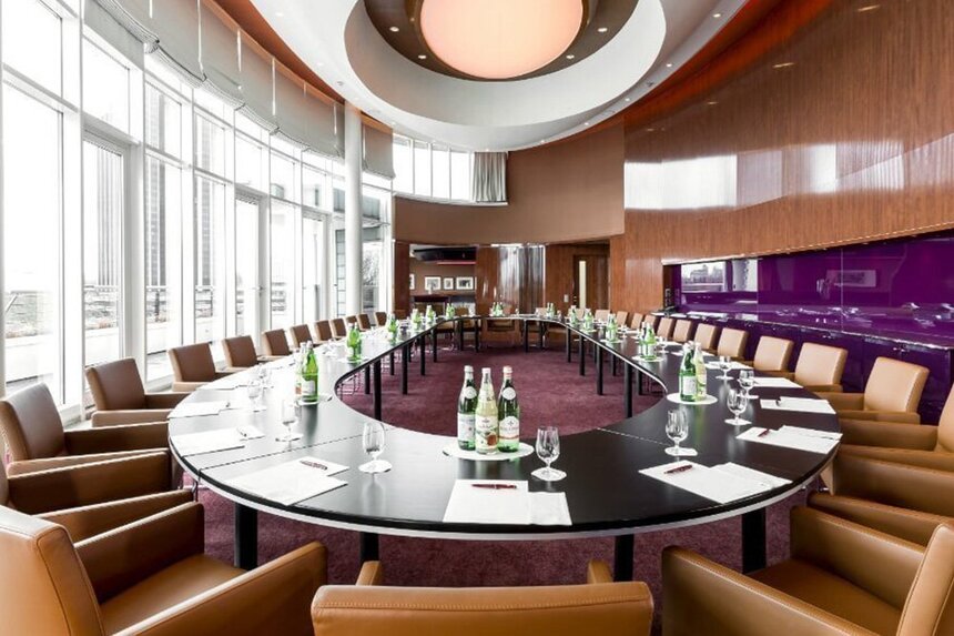 Großer Meetingraum in Holz- und Lilatönen mit ovalem, gedecktem Tisch und heller Fensterfront